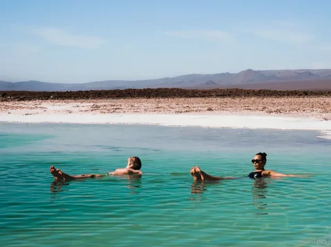 Atacama tours combo, two visitors floating in a turquoise salt lagoon with desert mountains behind