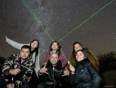 Atacama stargazing tours, smiling group posing under the night sky as green laser beams point at stars