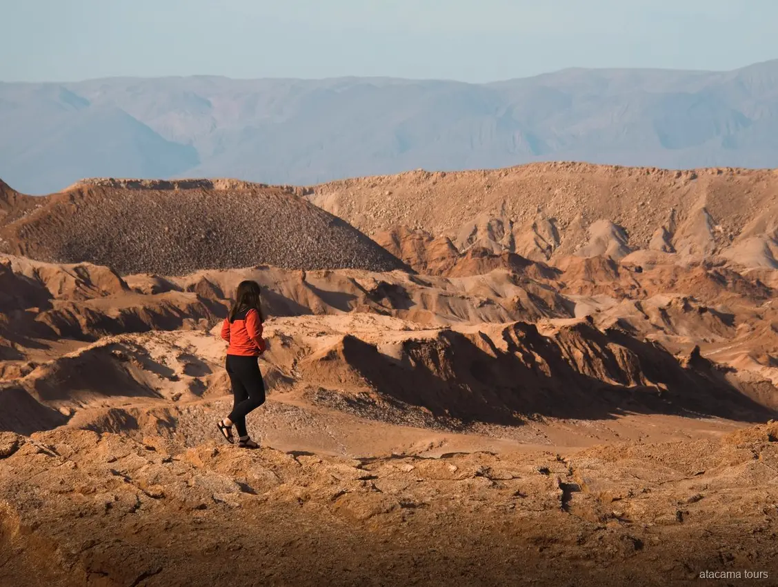Atacama tours to Baltinache, hiker in a red jacket overlooking eroded desert ridges and far mountains