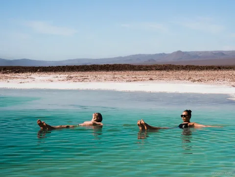 Excursions dans l'Atacama, deux visiteurs flottant dans une lagune salée turquoise face aux montagnes