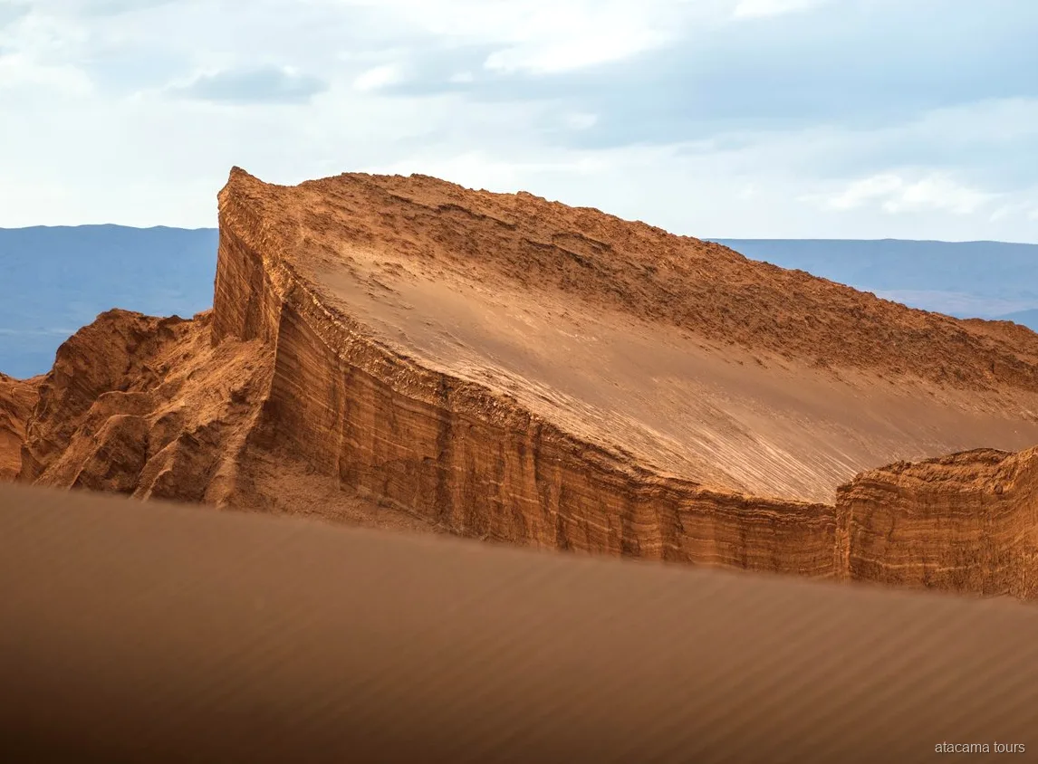 Atacama tours in Moon Valley, tilted layered rock wall rising above a rippled sand dune