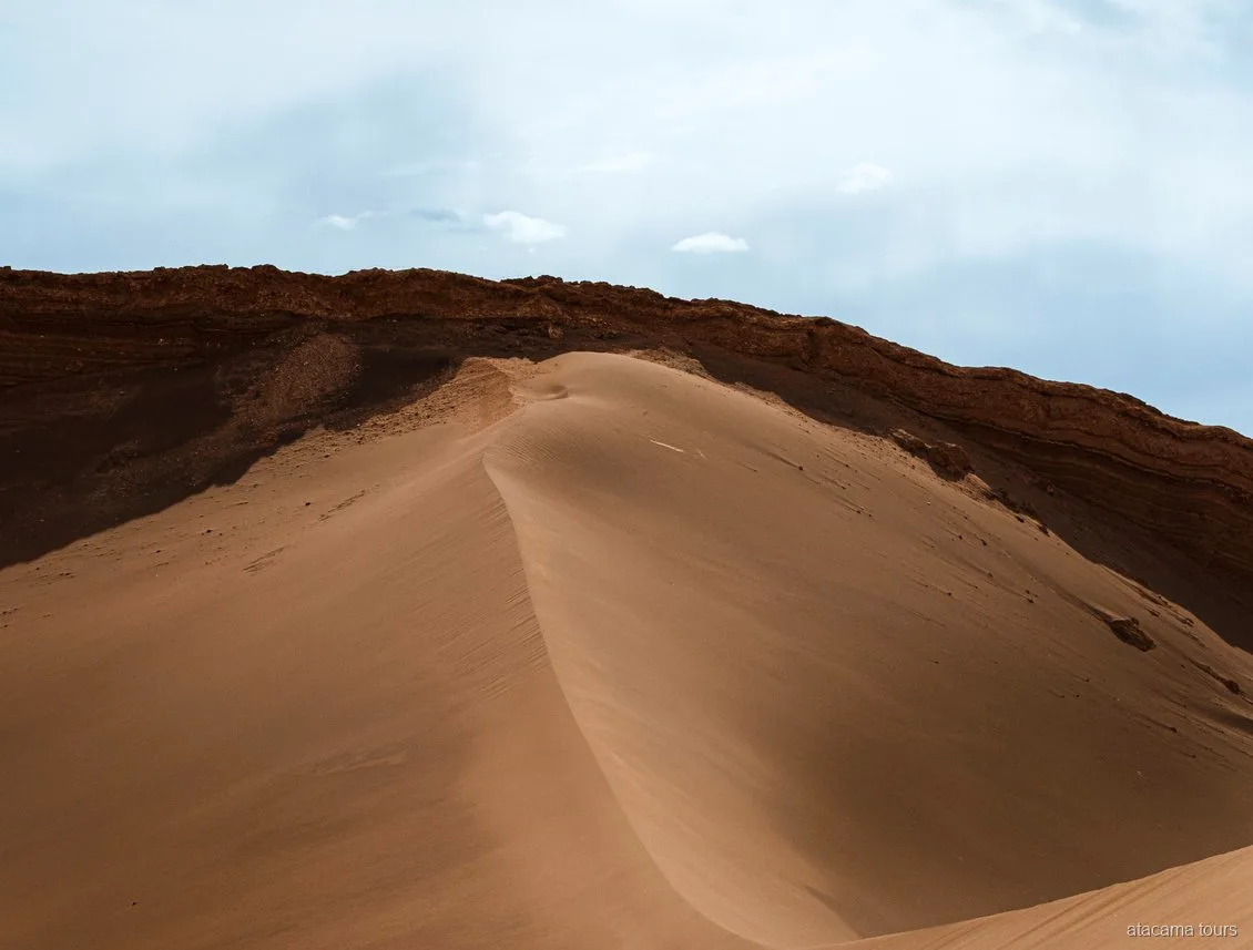 Atacama tours through Moon Valley, smooth sand dune curving below a dark layered rock ridge