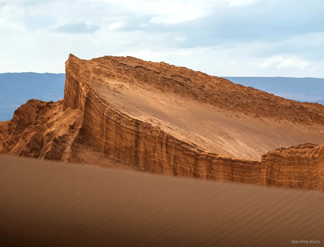 Passeios no Atacama pelo Valle de la Luna, paredão de rocha inclinado em camadas sobre uma duna ondulada