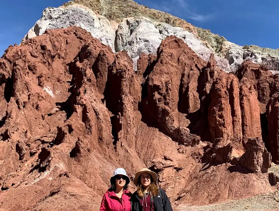 Atacama tours in Rainbow Valley, two visitors in sun hats before jagged red rock spires topped with white