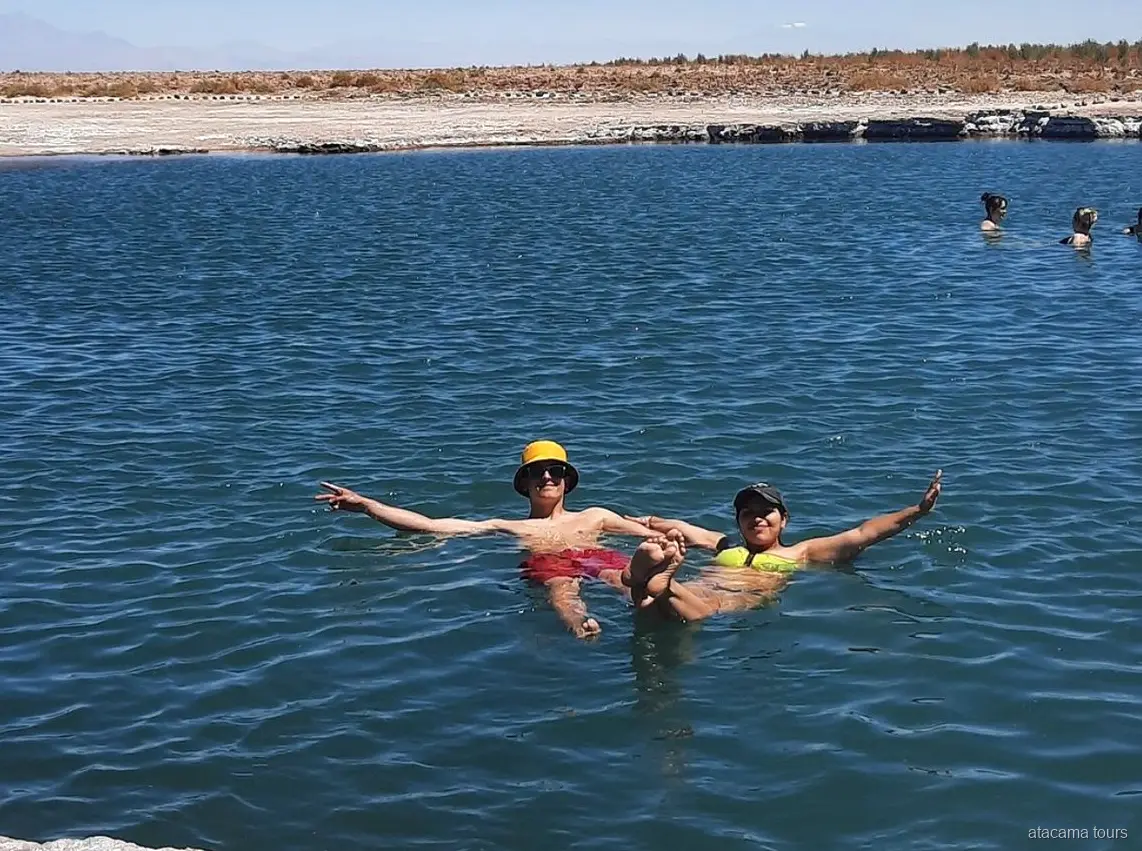 Tours en Atacama: dos visitantes flotan con los brazos abiertos en el agua salada de Laguna Cejar