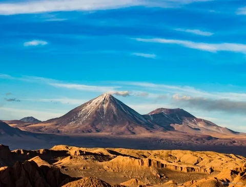 Paisagem dos passeios no Atacama, cone vulcânico com neve sobre cristas douradas e erodidas do deserto
