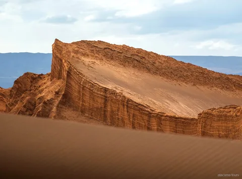 Tours en Atacama por el Valle de la Luna, pared de roca estratificada e inclinada sobre una duna ondulada