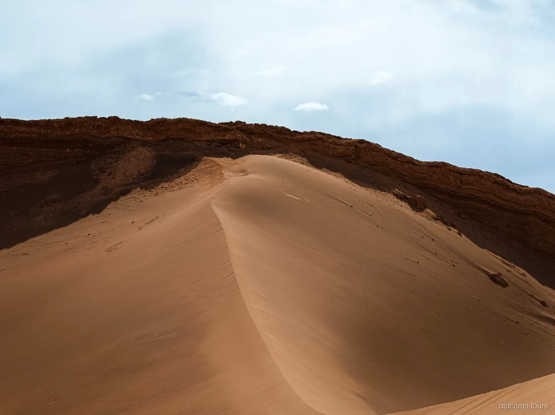 Tours en Atacama por el Valle de la Luna, duna de arena lisa que se curva bajo una cresta de roca oscura