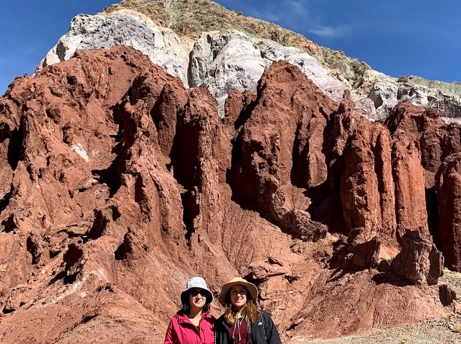 Tours en Atacama al Valle del Arcoíris, dos visitantes con sombrero ante agujas de roca roja coronadas de blanco