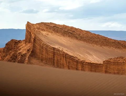 Excursions dans l'Atacama à la Vallée de la Lune, paroi rocheuse inclinée en strates au-dessus d'une dune