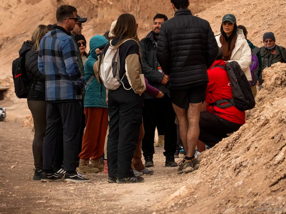 Groupe d'excursion dans l'Atacama en vestes chaudes réuni autour du guide sur un sentier de la Vallée de la Lune