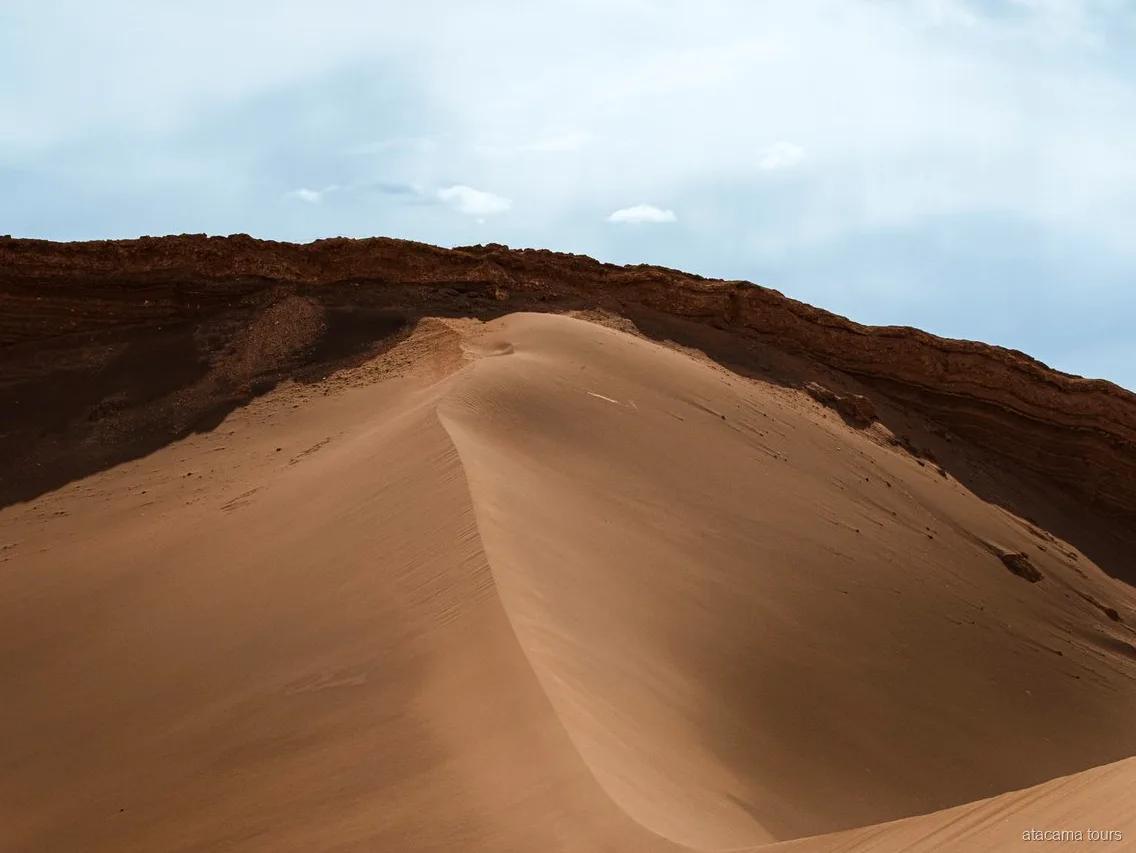 Excursions dans l'Atacama, dune de sable lisse sous une crête rocheuse sombre de la Vallée de la Lune