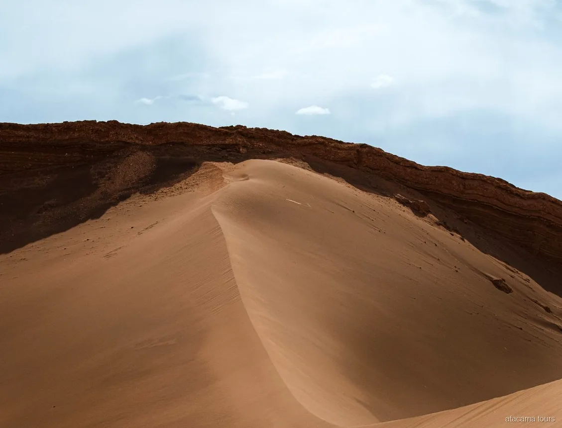 Atacama tours door de Valle de la Luna, gladde zandduin die buigt onder een donkere rotsrichel