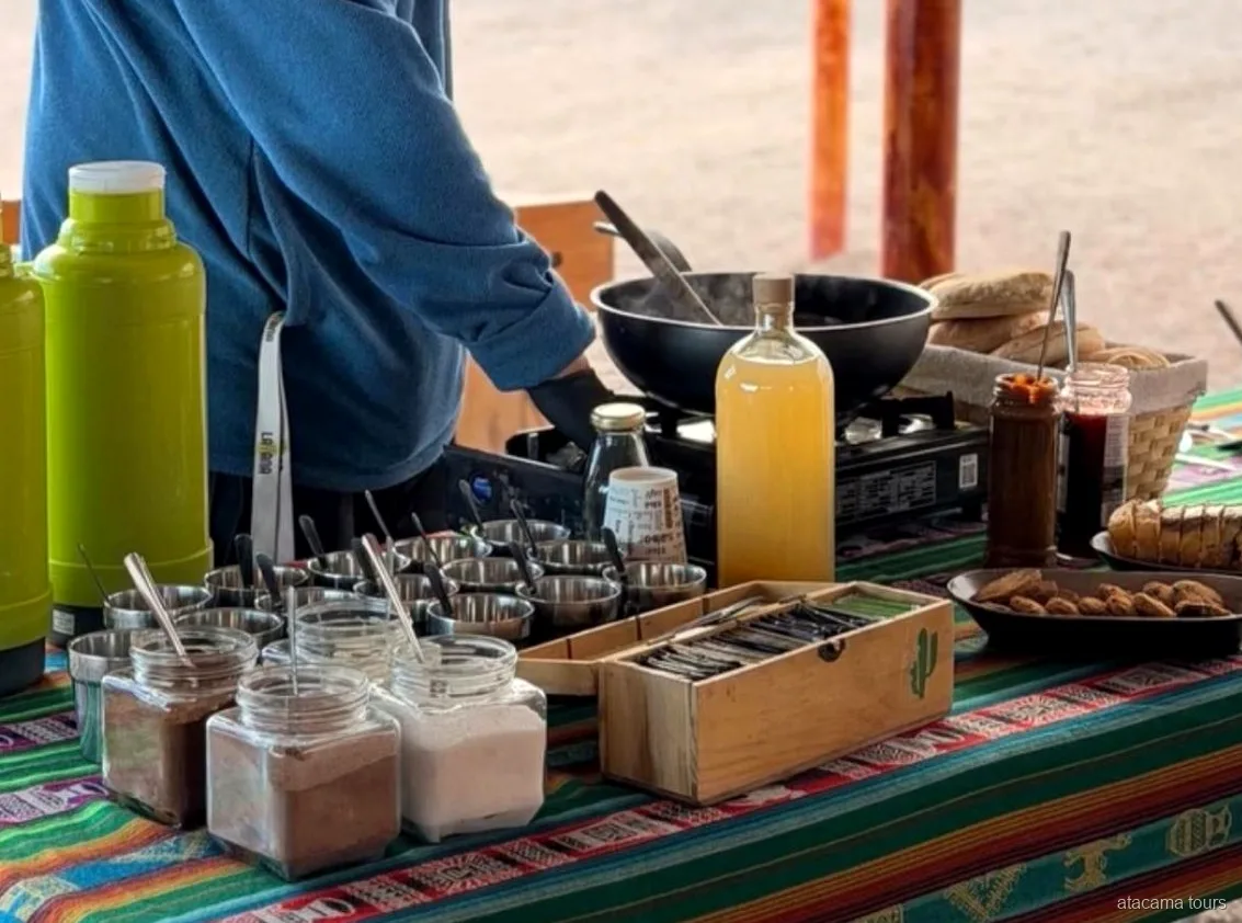 Snacktafel tijdens Atacama tours, thermosflessen, potten, brood en een kampeerbrander op een gestreept Andeskleed
